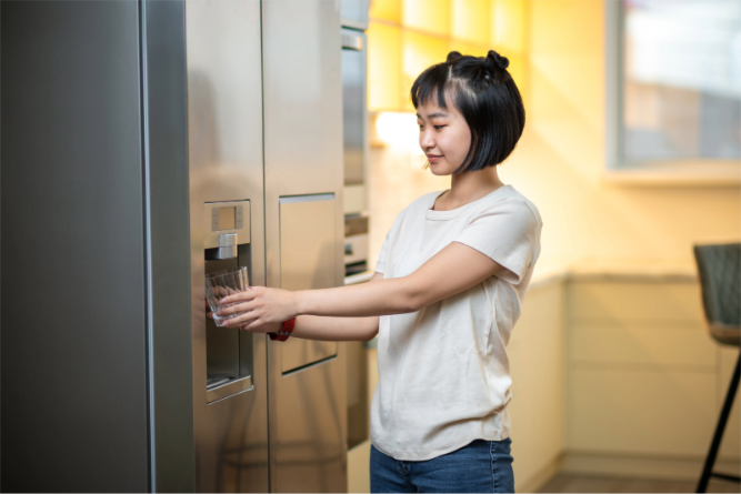 Homeowner filling a glass of drinking water from a refrigerator dispenser after installing a whole house backwashing carbon filter.