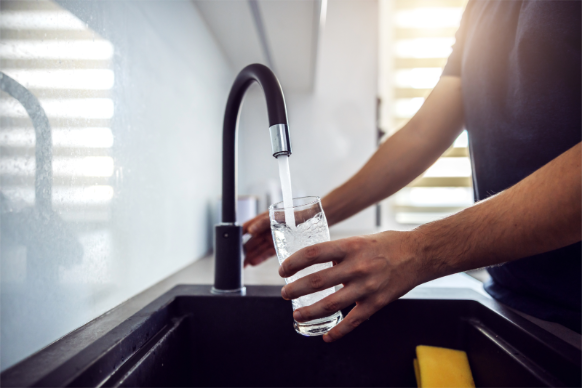 Homeowner filling a glass of clean drinking water from a kitchen faucet, highlighting improved Ohio water quality.
