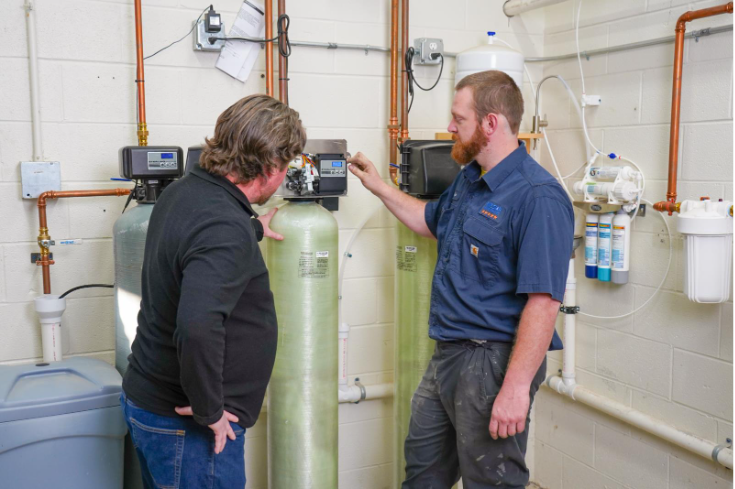 Plumber explaining water softener system settings to a homeowner, highlighting installation and overall water softener cost.