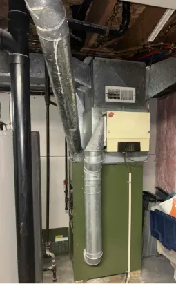 Old furnace system in a basement with exposed ductwork and pipes, a common example of equipment needing furnace replacement.